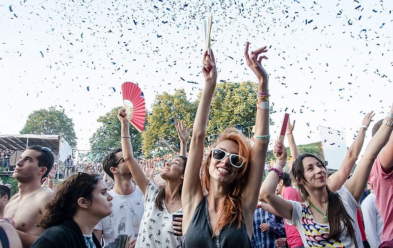 Teens throw their hands in the air with confetti surrounding them at a music festival. 