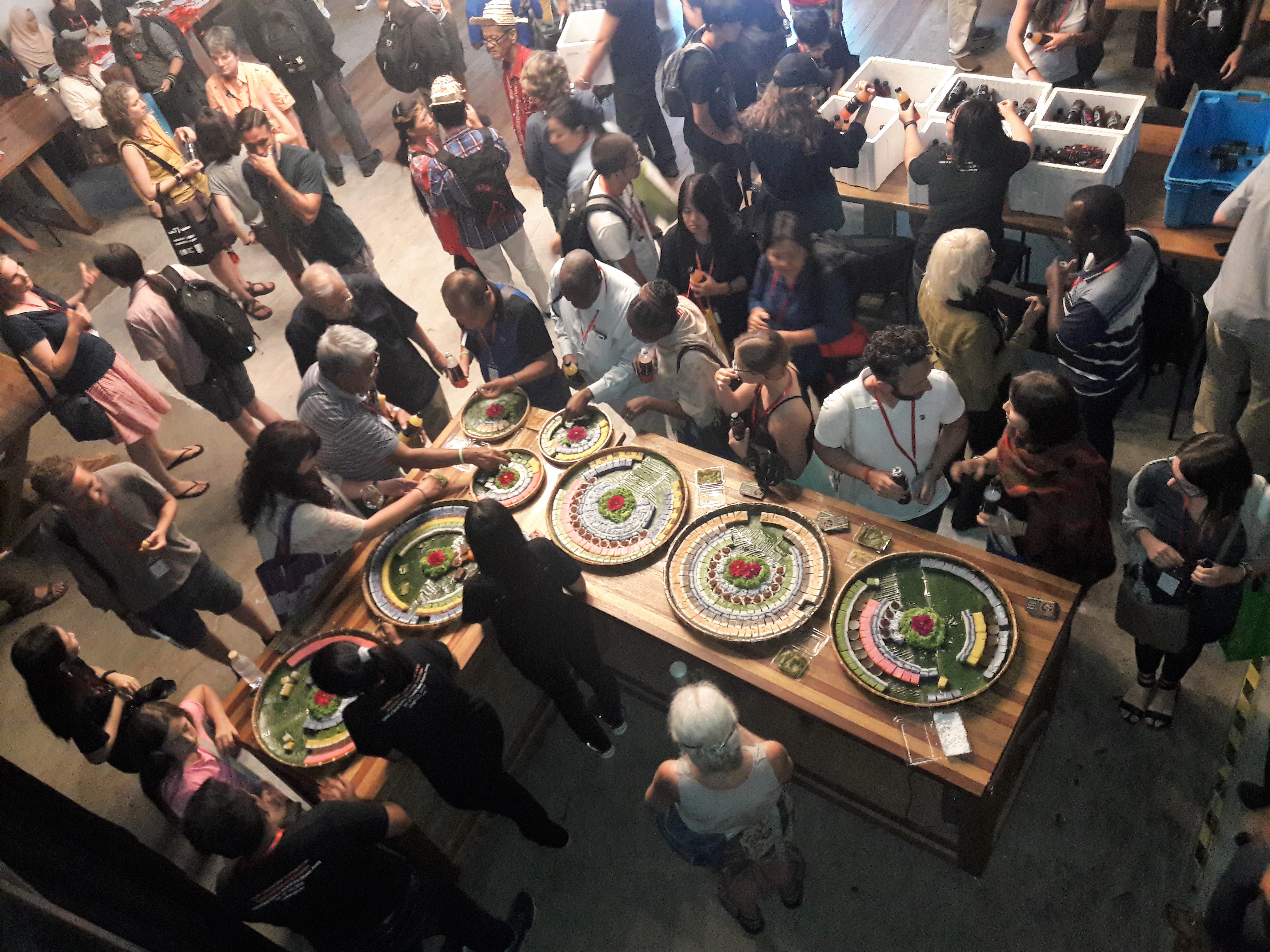 An L-shaped table with circular snack trays surrounded by people. 