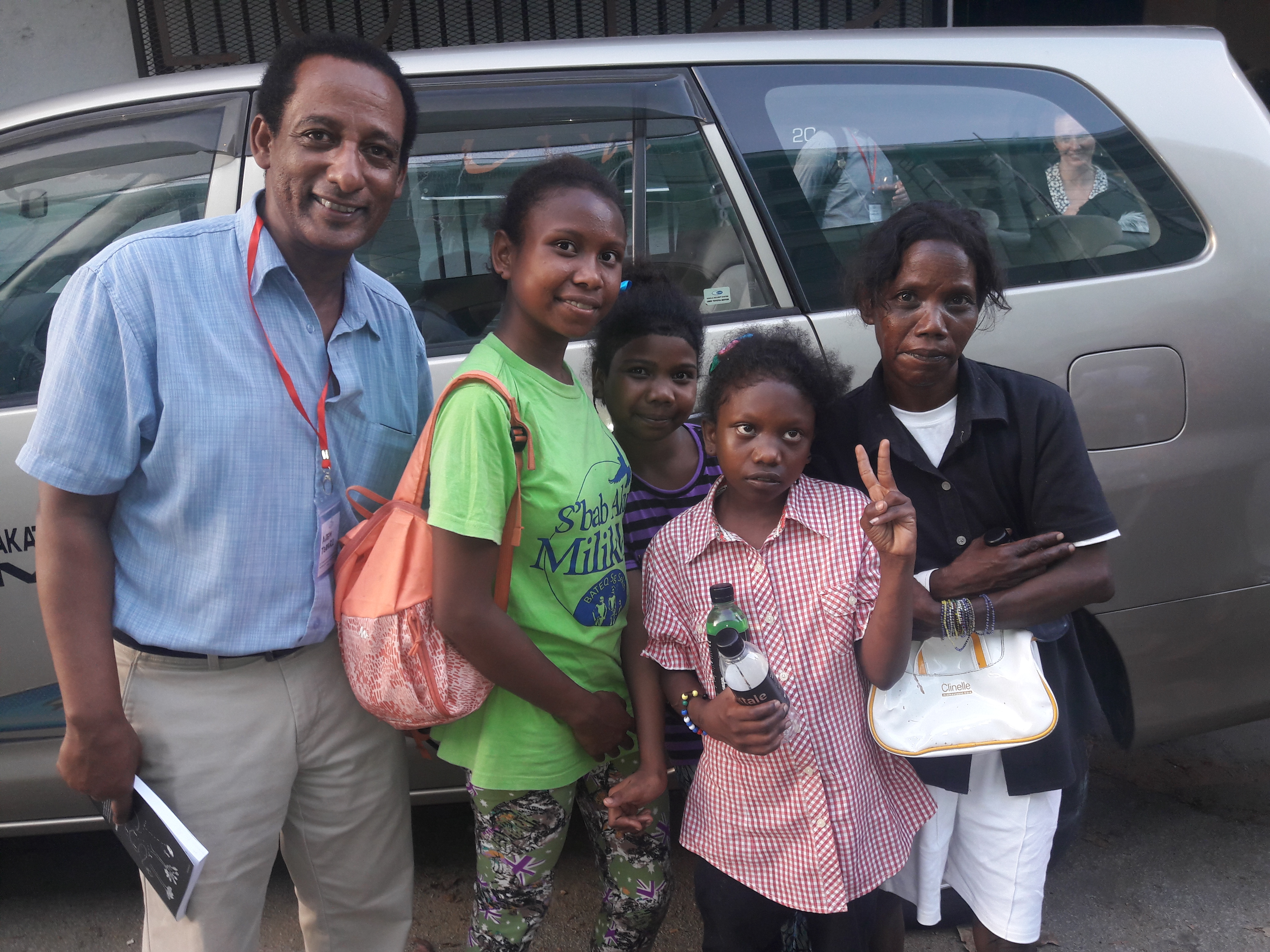 Teferi poses with a woman and three girls beside a car.